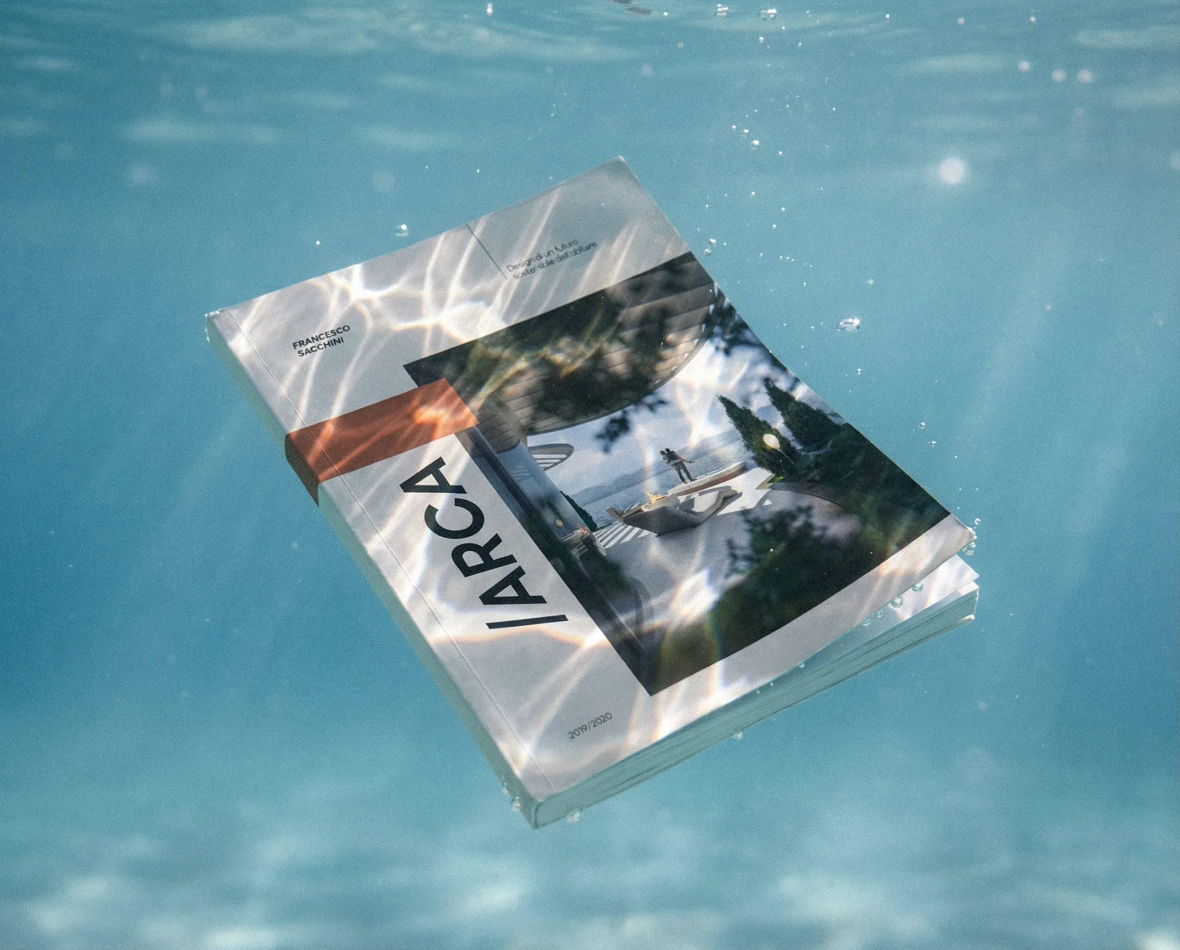 Libro di presentazione di ARCA in formato B5 sospeso sott'acqua, con la copertina fotografica e il titolo in verticale: mockup editoriale