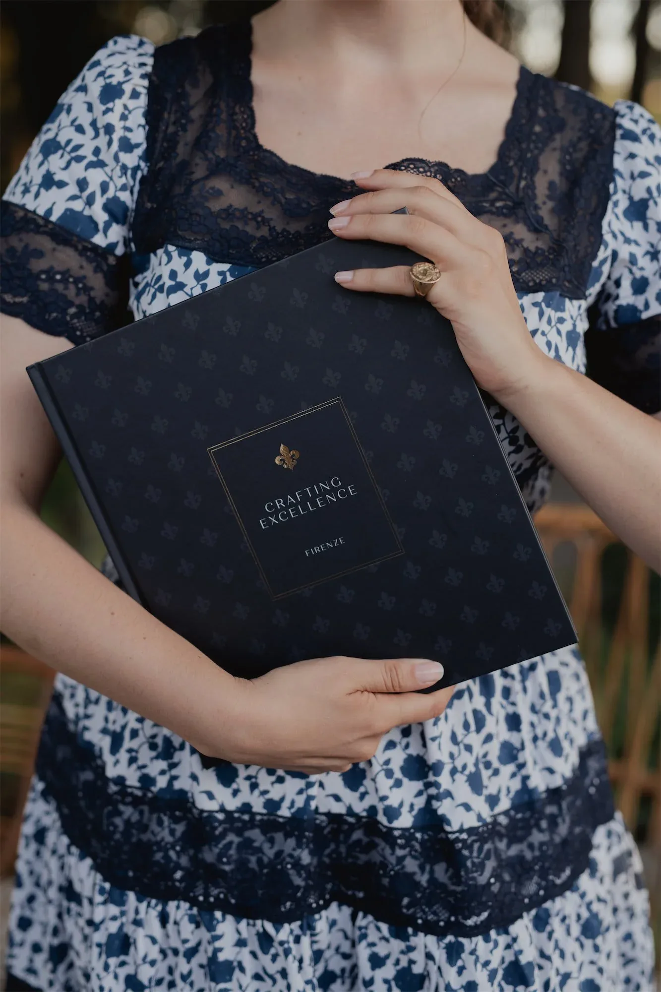 Il libro chiuso tenuto al petto da una donna in abito a fiori blu, con la copertina e il giglio in vista: fotografia dell'evento di presentazione