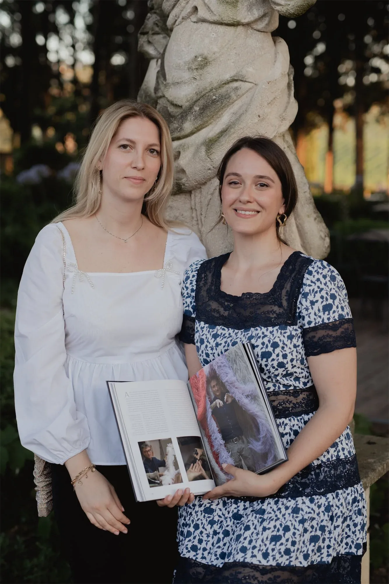 Due donne posano in giardino con il libro aperto fra le mani, una statua alle spalle: fotografia dell'evento di presentazione del libro