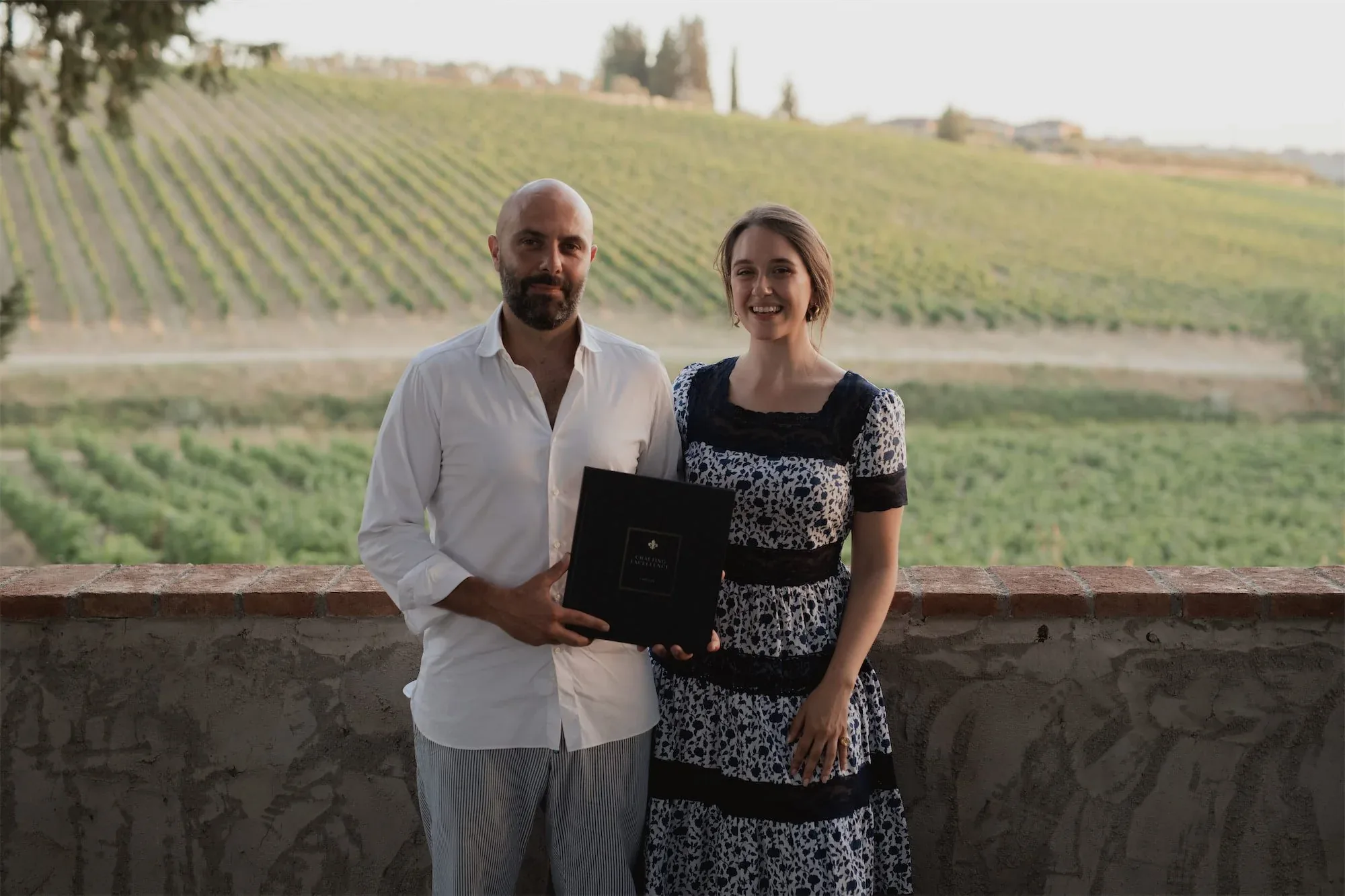 Un uomo e una donna posano con il libro su una terrazza affacciata sui vigneti: fotografia dell'evento di presentazione del libro