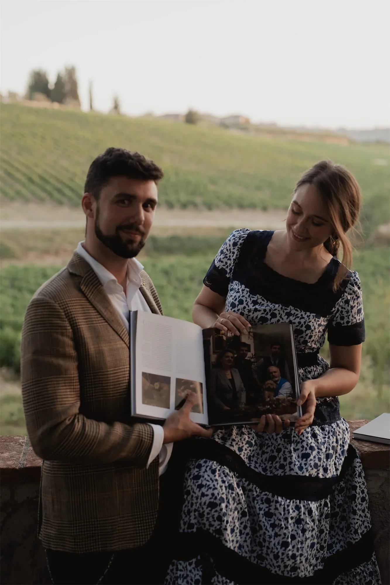 Un uomo e una donna sfogliano il libro aperto con i vigneti sullo sfondo: fotografia dell'evento di presentazione di Crafting Excellence