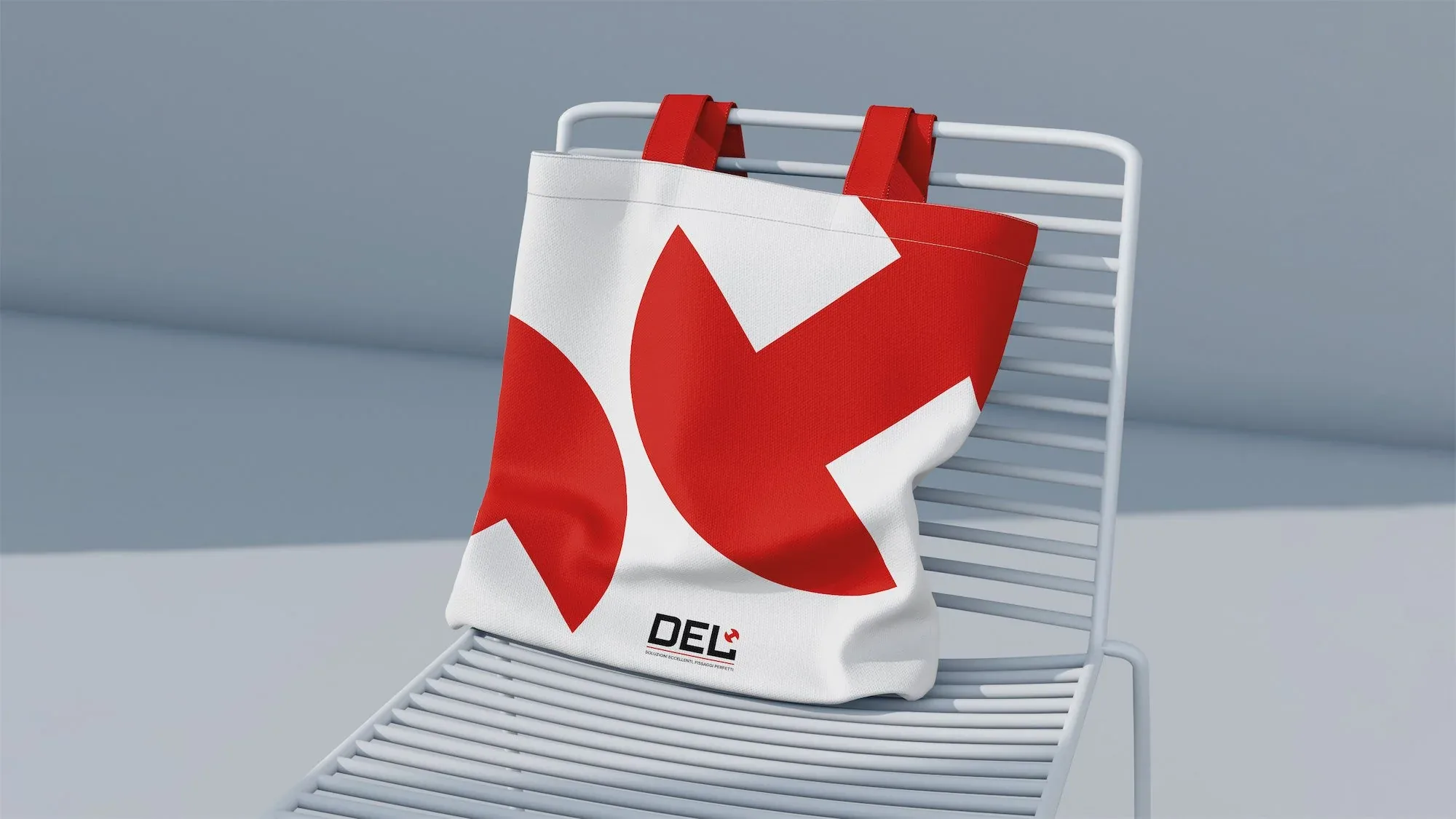Shopper bianca con il pittogramma rosso del logo DEL in grande, appoggiata su una sedia in metallo: mockup di merchandising del rebranding