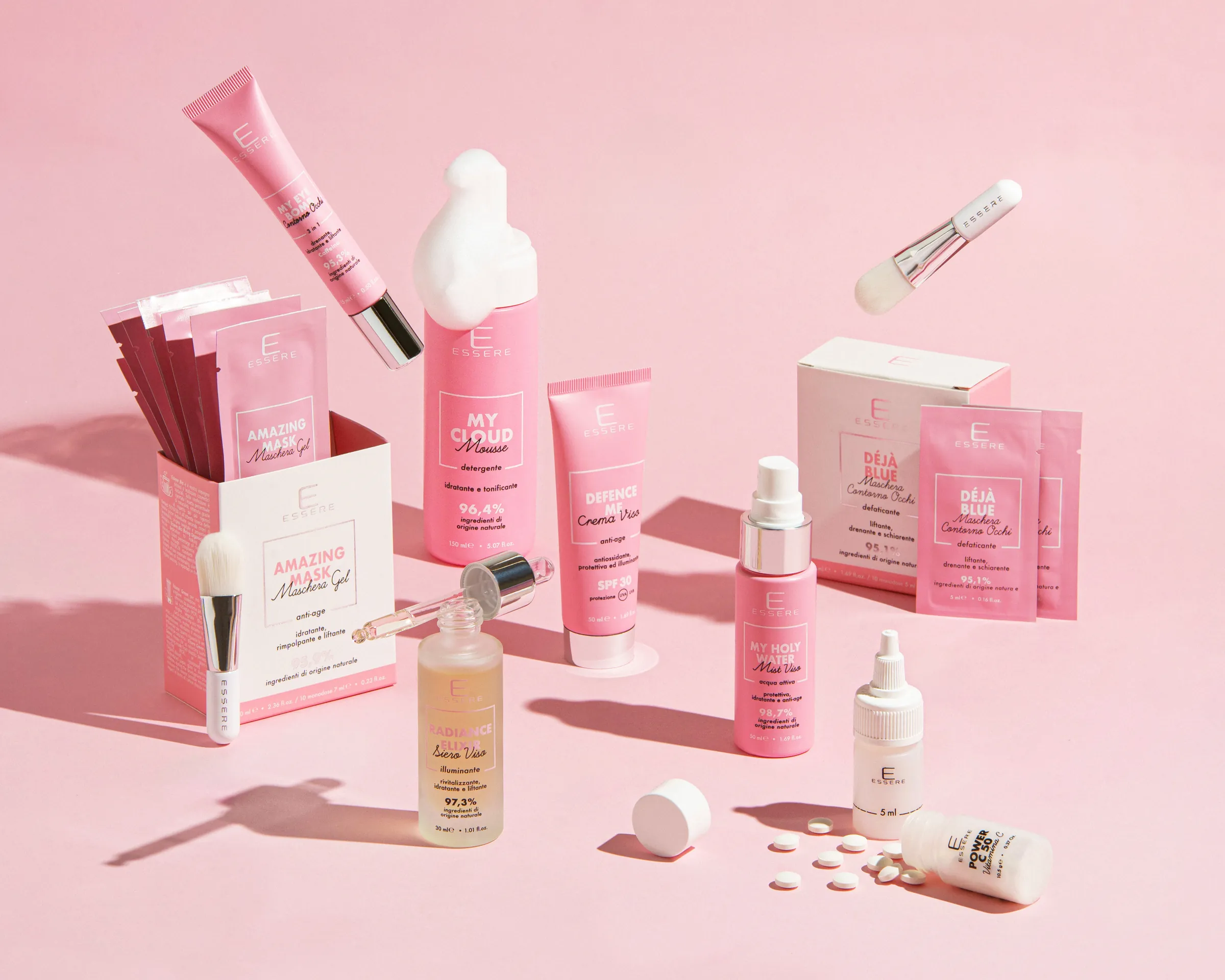 La linea viso di Essere Bio su fondo rosa: flaconi, tubetti, maschere in bustina e pennelli sospesi nella luce. Foto di copertina del progetto e-commerce e social