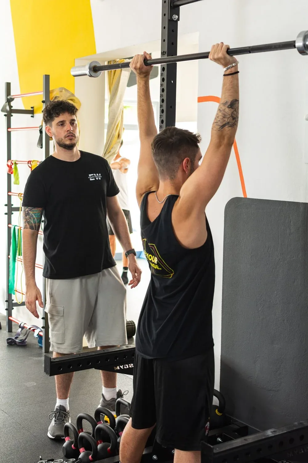 Ragazzo che si appende alla sbarra per le trazioni mentre un istruttore lo osserva: foto dallo shooting in studio per Etruria Wellness