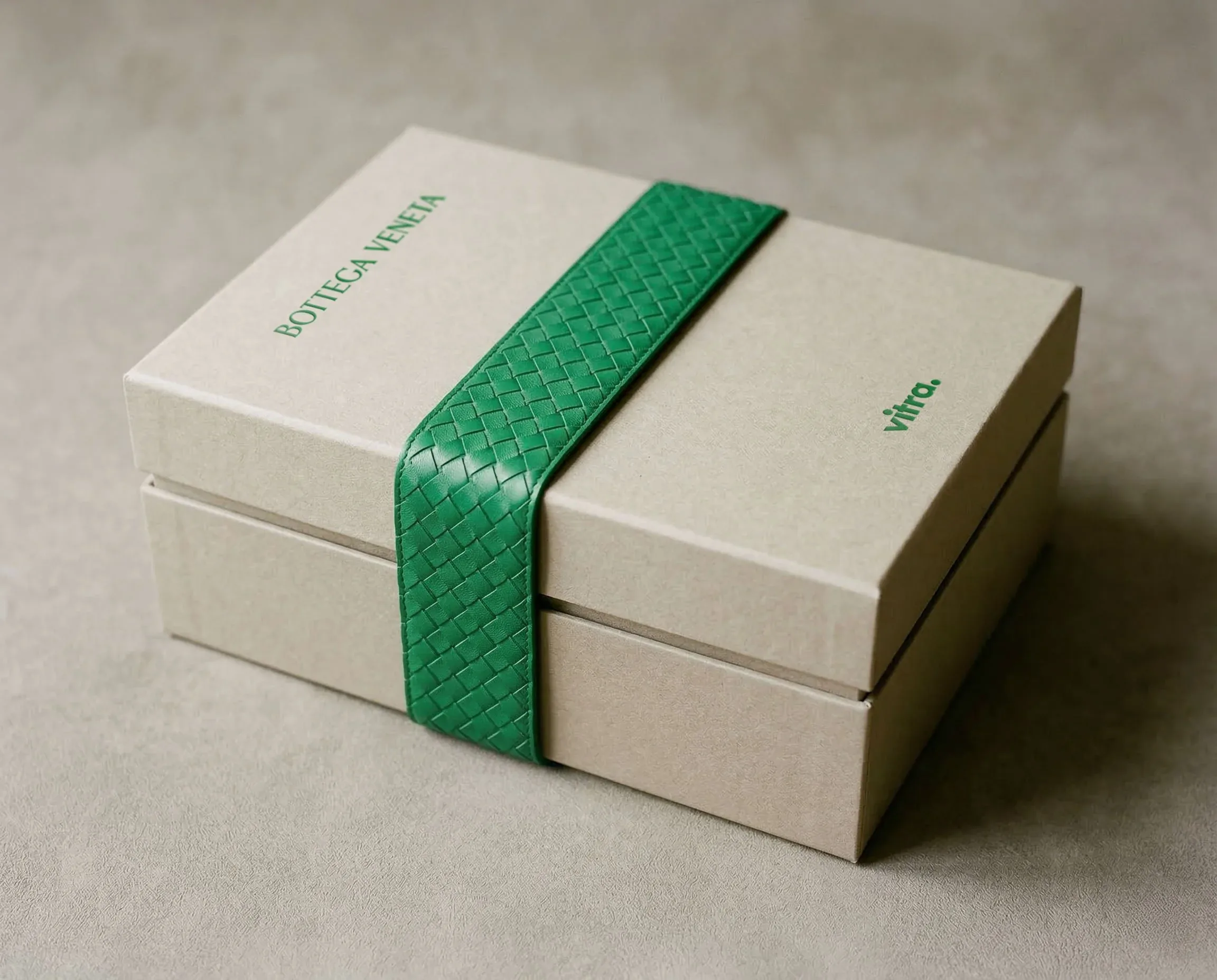 Cofanetto chiaro chiuso da una fascia in intrecciato verde, con i nomi Bottega Veneta e Vitra: mockup del press kit The Certification di Evergreen