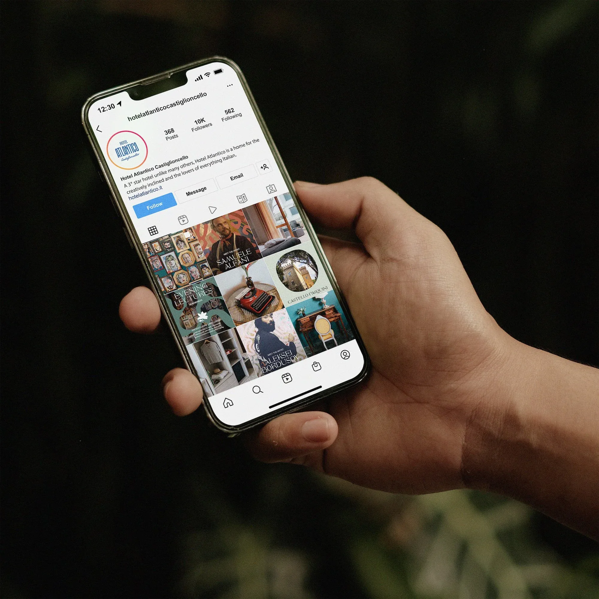 Mano che regge uno smartphone con il feed Instagram di Hotel Atlantico su fondo scuro: contenuti social per la stagione estiva dell'hotel
