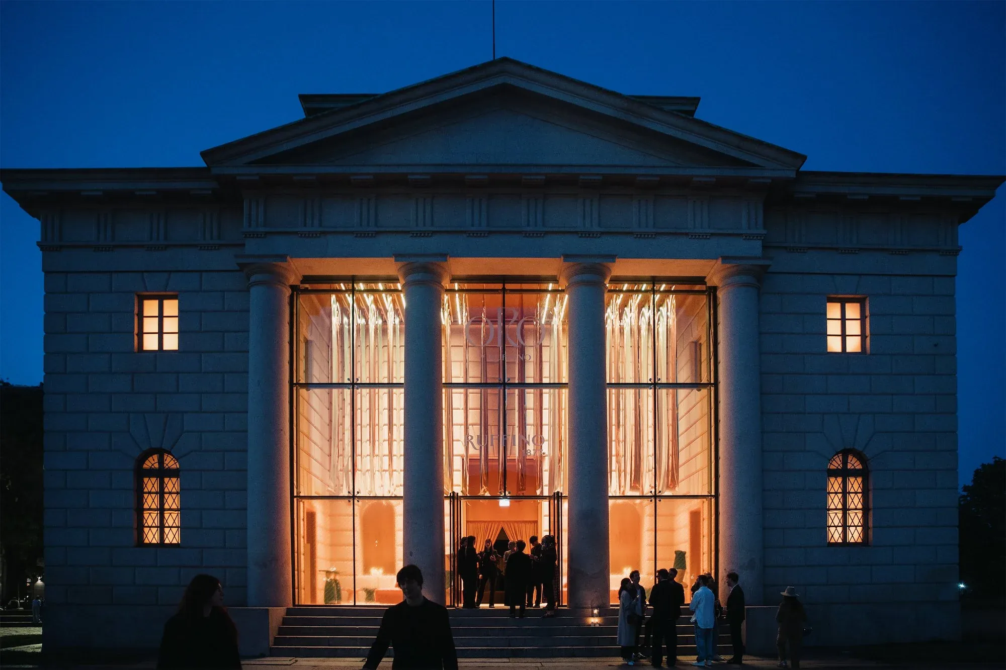 Facciata neoclassica a colonne illuminata all'ora blu, con gli ospiti sui gradini: la location di ORObyRUFFINO alla Milano Design Week 2024