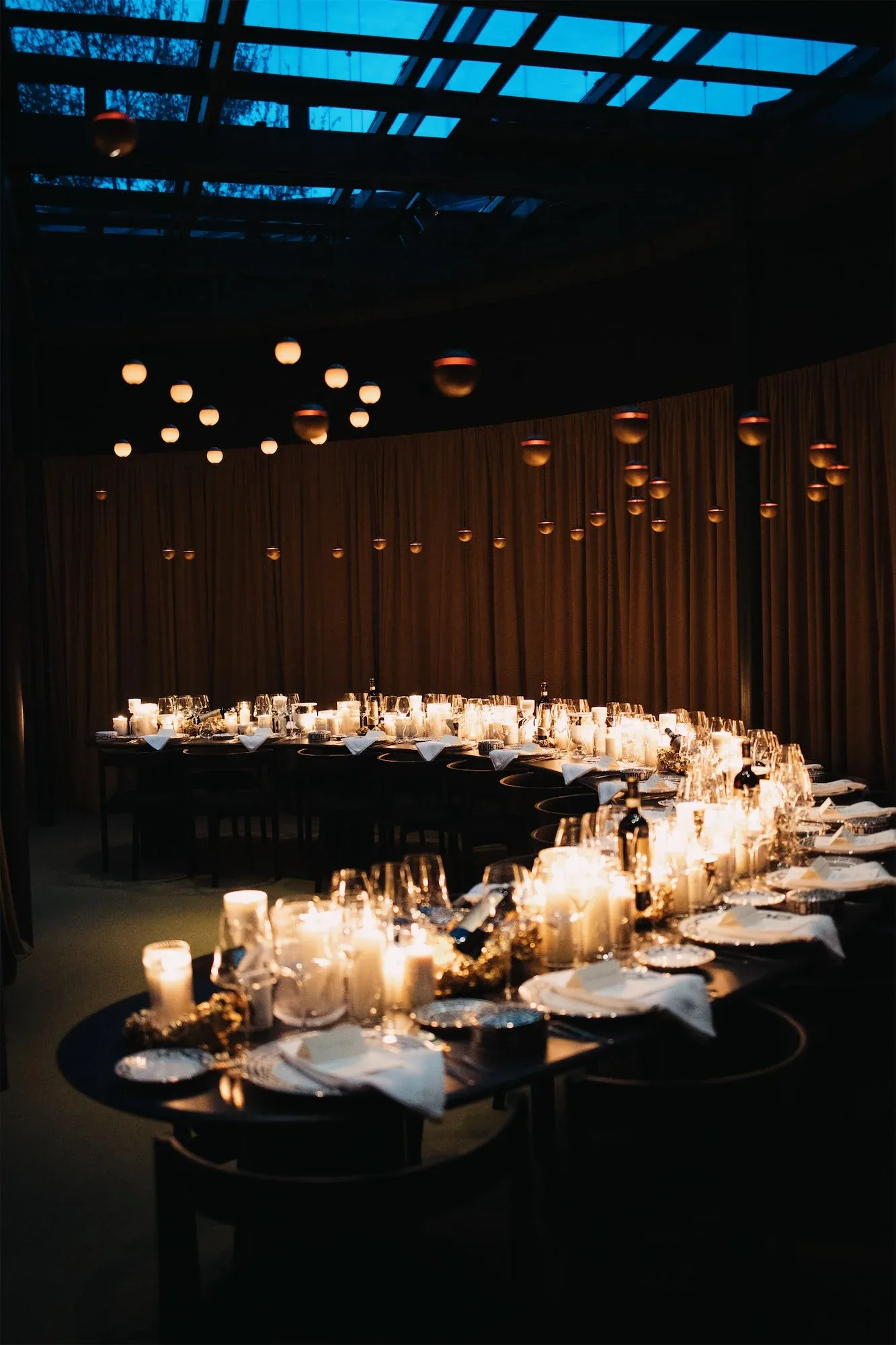 Lunga tavolata curva illuminata dalle candele in una sala scura con lucernario, la cena di opening di ORObyRUFFINO alla Milano Design Week 2024