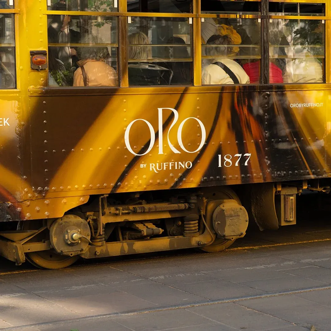 Fiancata del tram con il logo ORO by Ruffino 1877 su onde d'oro e passeggeri al finestrino: rivestimento tram per la Milano Design Week 2024