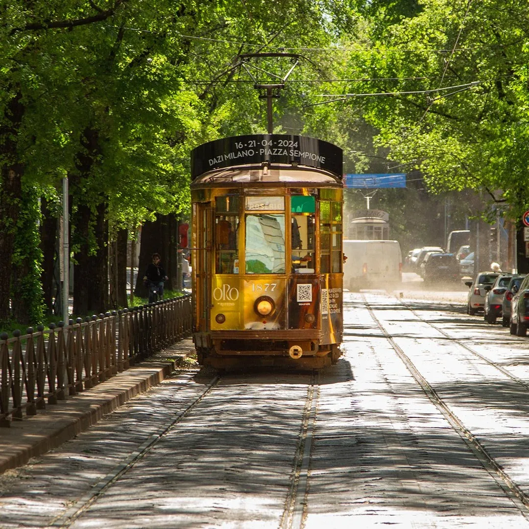 Tram con il rivestimento dorato ORO by Ruffino che avanza in un viale alberato di Milano: grafica per la comunicazione di ORObyRUFFINO 2024