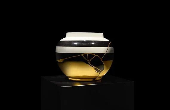 Vaso bianco con fasce scure e riflessi d'oro su un piedistallo nero, l'opera di Chiara Lorenzetti esposta a ORObyRUFFINO 2024