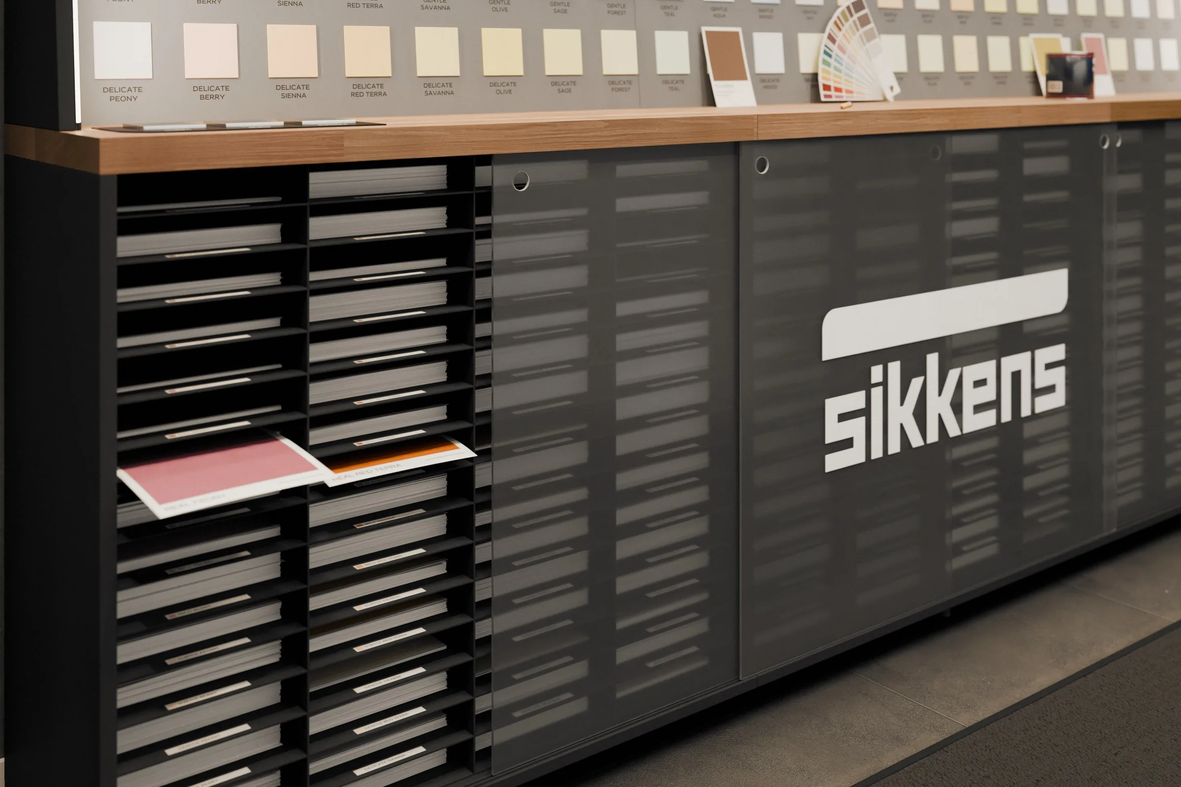 Le ante in plexi sabbiato col logo Sikkens e una aperta sui ripiani dei fogli colore A4, con un foglio sfilato. Render 3D